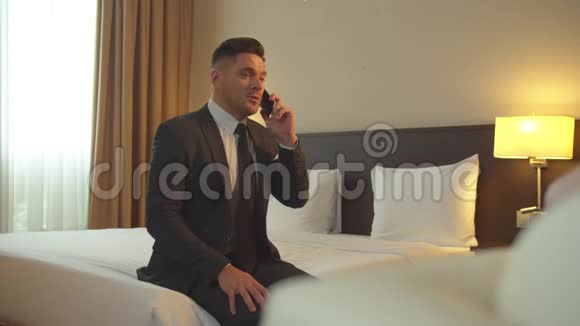 穿西装的男人坐在床上在旅馆里打电话视频的预览图