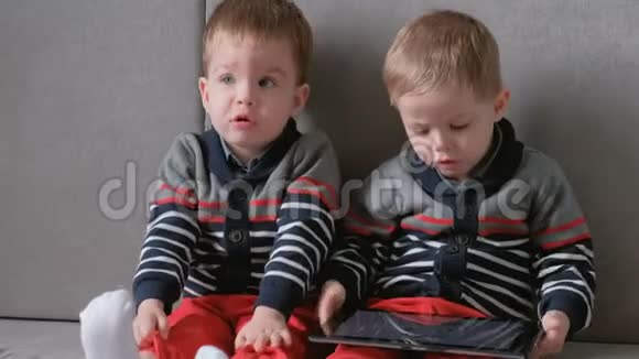 两个孪生兄弟蹒跚学步坐在沙发上的平板电脑上一起玩游戏视频的预览图