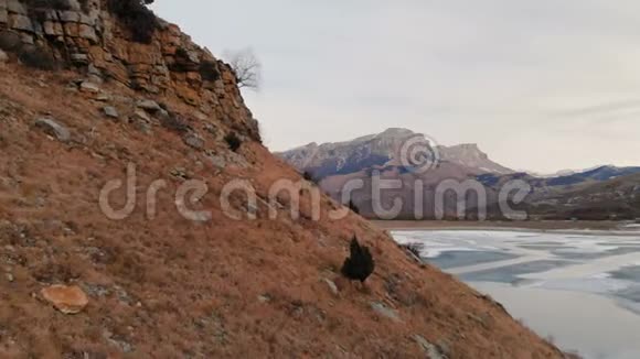 以史诗般的岩石和悬崖为背景在冻结的山湖畔鸟瞰山坡和悬崖视频的预览图