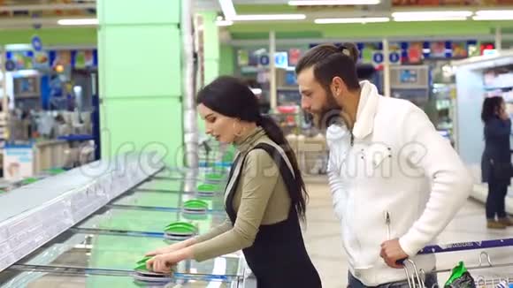 可爱的白种人夫妇从超市冰箱里选择冷冻食品视频的预览图