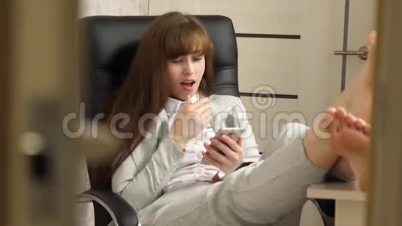 有电话的漂亮女商人坐在椅子上光着脚在桌子上休息在办公室工作的女孩视频的预览图