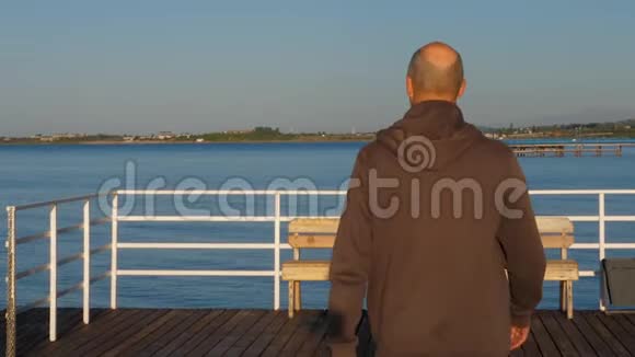 成年男子漫步在蓝色的码头湖水上眺望风景视频的预览图