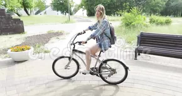 带背包的快乐女孩在公园里骑自行车视频的预览图