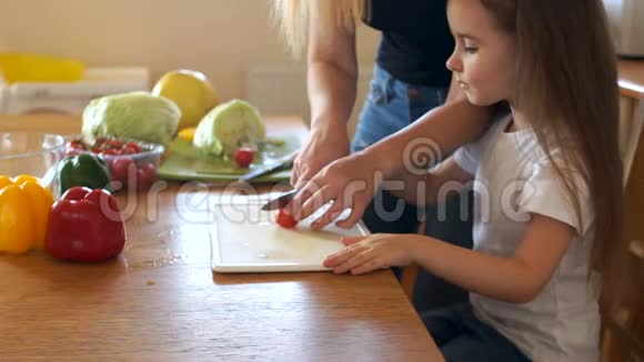 关爱的母亲教她的小女儿切蔬菜做沙拉素食樱桃番茄视频的预览图