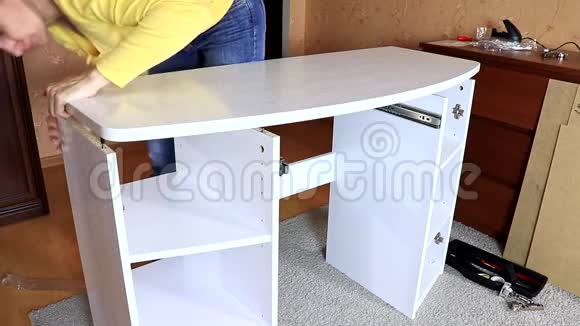 一个女人在搬新的白色家具她把一个桌面放在另一个半组装的梳妆台上视频的预览图