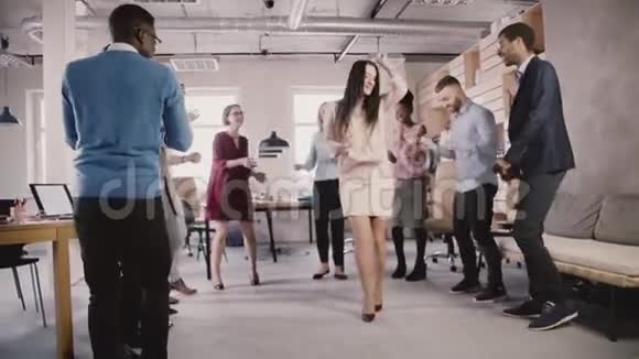 开朗的女商人在休闲的办公室团队建设聚会上跳舞多民族团队一起分享欢乐时光慢动作视频的预览图
