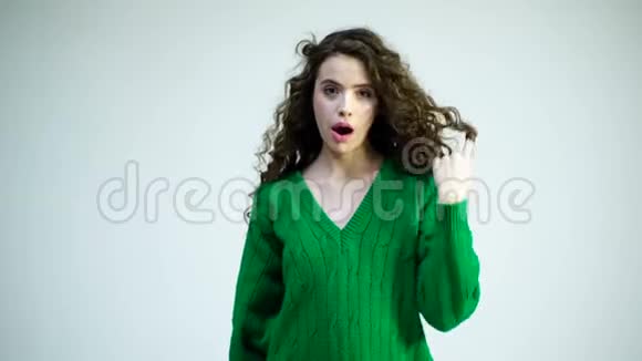 一个穿着绿色毛衣戴着牙套的卷曲女孩把头发包在手指上巴黎时尚化妆发的复古女郎视频的预览图