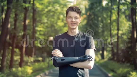 带着未来主义仿生假肢的青少年男孩站在公园里对着镜头微笑视频的预览图