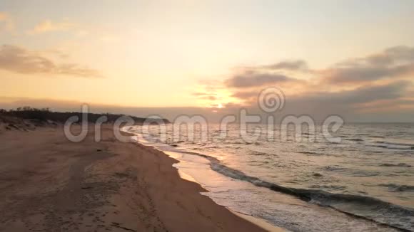 空中观看无人机镜头低飞行在一个废弃的海滩上日落带着滚滚海浪和夕阳的沙岸视频的预览图