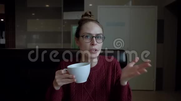 可爱的戴着眼镜的年轻女人坐在咖啡馆里和别人说话视频的预览图