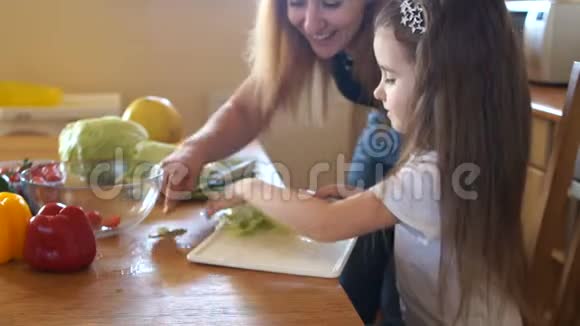 女儿和妈妈在厨房一个女孩帮她妈妈准备沙拉一个女人尝试卷心菜素食绿色视频的预览图