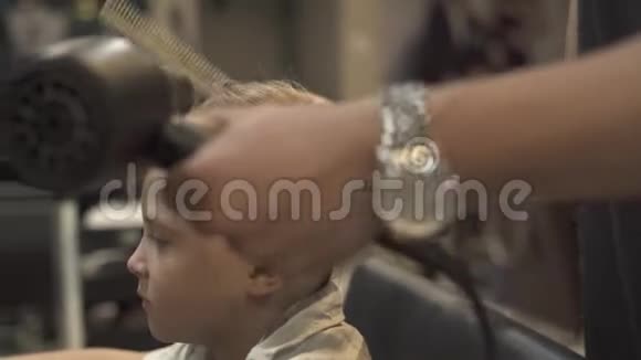 发型师在理发店用烘干机做男孩发型儿童美发沙龙晾晒头发美容师视频的预览图