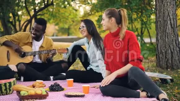 快乐的非裔美国人正在弹吉他而他的朋友们正围着他唱歌在公园野餐视频的预览图