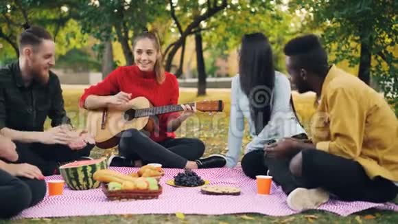 许多朋友在公园里唱歌拍手美丽的女孩在野餐时弹吉他视频的预览图