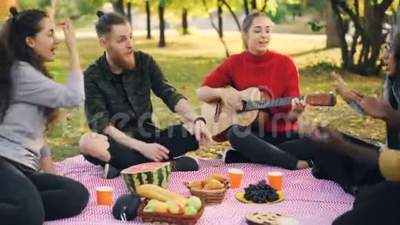 当他们的朋友漂亮的女孩在野餐时弹吉他时兴奋的女孩和男人在唱歌和拍手视频的预览图