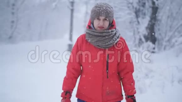 在白雪皑皑的背景下年轻美丽的女人在冬季公园散步的肖像在冬天的背景下看相机视频的预览图