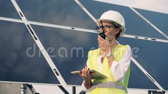 女工程师正站在太阳能电池板旁用对讲机交谈替代能源概念视频的预览图
