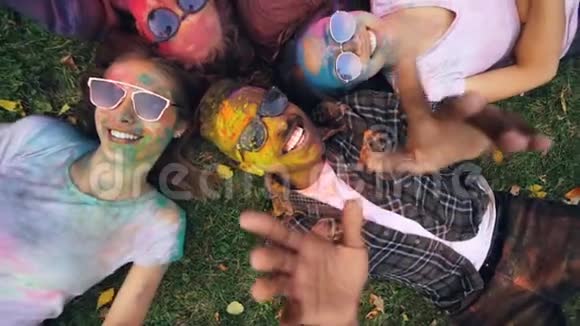 远离快乐的朋友多种族的群体在聚会后躺在草地上五颜六色的脸和衣服在动视频的预览图
