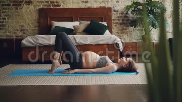 漂亮的孕妇穿着舒适的孕妇装在卧室的瑜伽垫上做运动健康视频的预览图