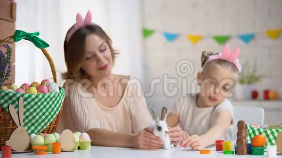小女孩在妈妈手里玩可爱的小兔子宠物复活节的象征视频的预览图