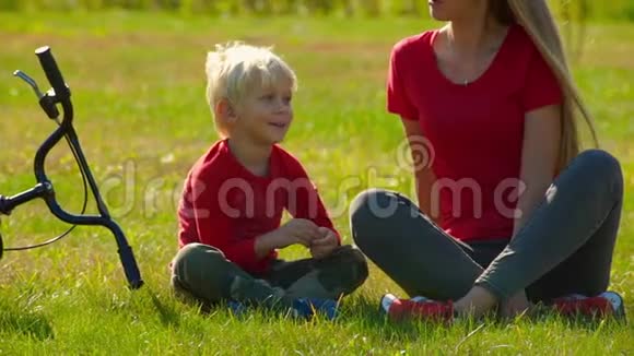一个年轻的女人和她的小儿子坐在草坪上旁边放着一辆自行车视频的预览图