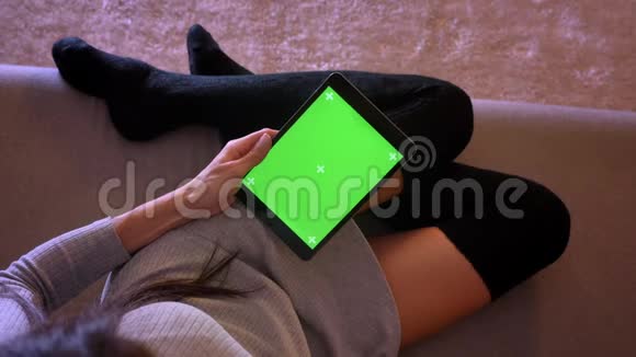 用绿色屏幕在平板电脑上播放视频的年轻漂亮女性的特写肖像女孩的腿在舒适的位置视频的预览图