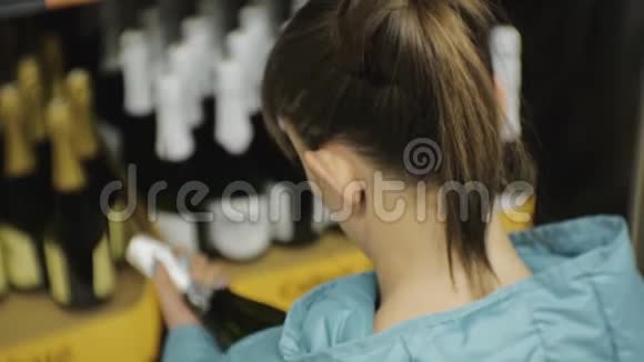 超市里的女人穿蓝色夹克的年轻白种女人看黑瓶上的标签视频的预览图