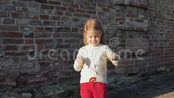 小女孩在一根棍子上抿着红唇站在砖墙旁边视频的预览图