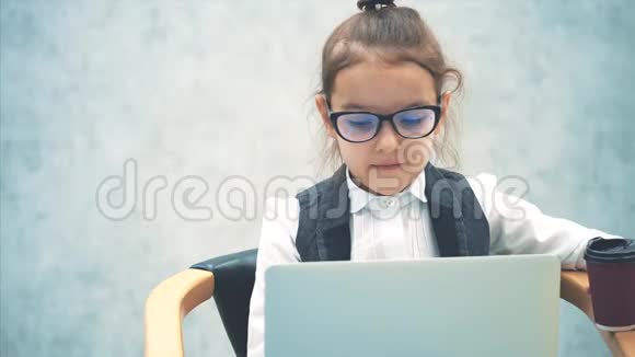 小商业女孩微笑着看灰色背景在此期间笔记本电脑被保存坐在椅子上视频的预览图