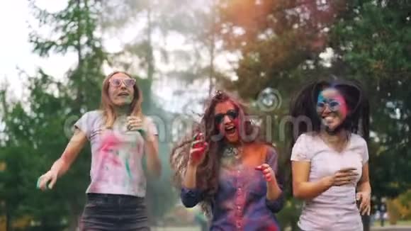 在霍利节上穿着时髦的服装快乐的女孩在粉末涂料的云彩中跳舞和欢笑视频的预览图