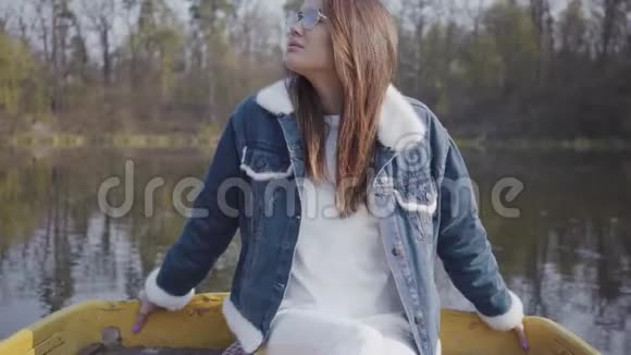 肖像漂亮的年轻女子戴着时髦的眼镜和牛仔裤夹克看着镜头美丽的风景视频的预览图