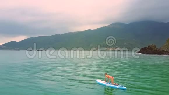 金发女人躺在海洋桨板上的瑜伽姿势视频的预览图