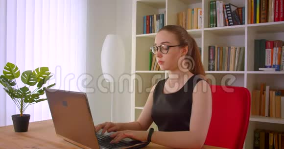 年轻漂亮的红发女商人戴着眼镜在办公室室内使用笔记本电脑的特写肖像视频的预览图