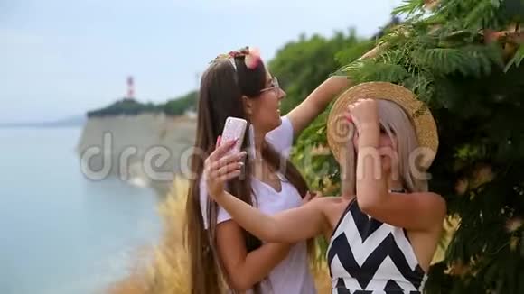 两个积极的女孩一个戴着帽子的金发女孩一个戴着眼镜的黑发女孩四处闲逛用手机拍自拍视频的预览图
