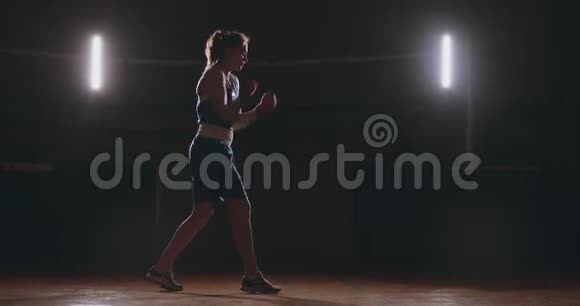一个漂亮的女拳击手在黑暗的健身房训练并在缓慢的运动中锻炼出拳头相机运动侧视图Stadicam视频的预览图