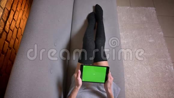 室内沙发上穿着可爱袜子的女腿特写镜头女人在平板电脑上玩绿色电子游戏视频的预览图