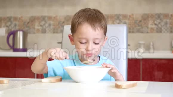 孩子坐在白色的厨房桌子旁吃面包和汤视频的预览图