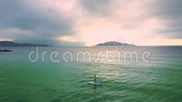 女人在岛后的粉红色天空上划着桨视频的预览图