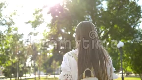 一个背着背包的女孩带着耳机在公园里散步听着音乐微笑着挥动着她的手挥手视频的预览图
