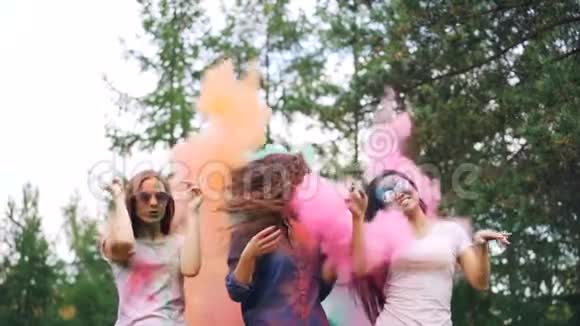 当人们向她们投掷五颜六色的面粉时快乐的年轻女士在粉末涂料的云中翩翩起舞视频的预览图