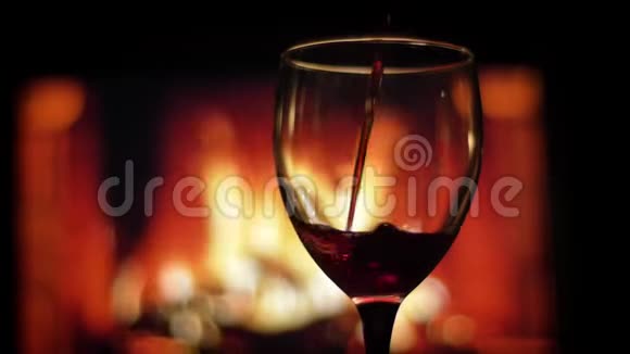 将红酒倒入空杯中的特写镜头背景上有温暖的壁炉和火焰视频的预览图