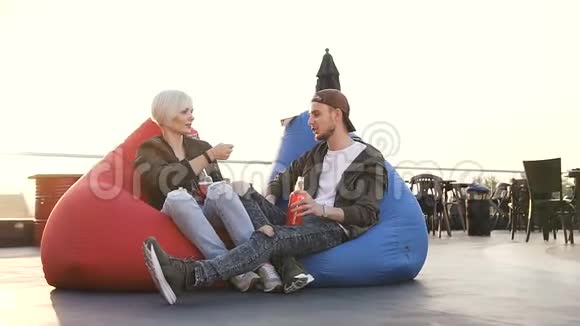 年轻人和女孩坐在露台咖啡馆的多色扶手椅上喝能量饮料朋友喝点酒视频的预览图