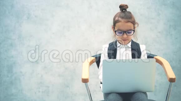 小商业女孩微笑着看灰色背景在此期间笔记本电脑被保存坐在椅子上视频的预览图