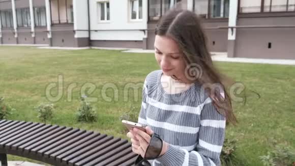 漂亮的黑发女人在手机上聊天和打字坐在长凳上微笑视频的预览图