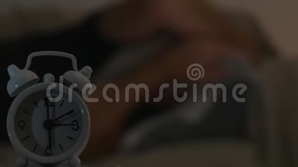 一个疲惫的人睡在床上闹钟在前面的模糊图像视频的预览图