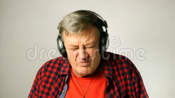 有表现力的成年老人听耳机上的音乐边唱歌边拍音乐视频的预览图