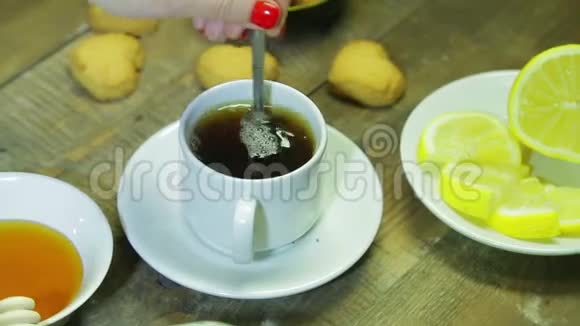 女人在木桌上的白色杯子里搅拌勺子鲜酿红茶视频的预览图