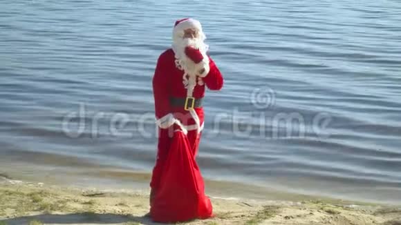 圣诞老人拿着一袋礼物站在河边或湖边视频的预览图