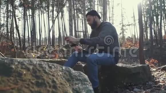 大胡子的人在森林里砍斧子粗鲁的男人坐在户外用斧头视频的预览图