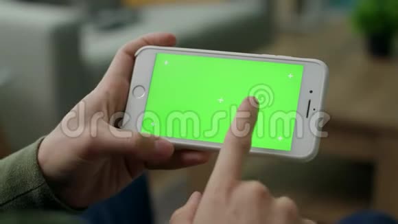 一个男人在智能手机上选择一个角色客厅里有一个绿色的屏幕视频的预览图